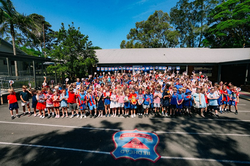 Students and players pose in front of a banner at Redhead Public School.